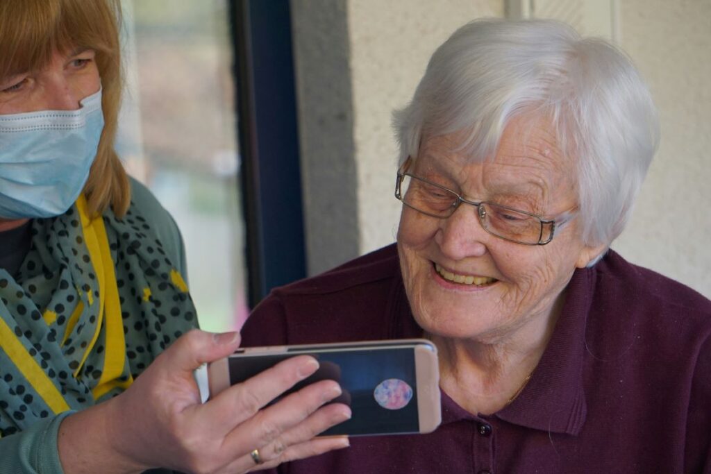 Mulher mostrando a uma pessoa idosa a tela de um celular. Foto de Foto de Georg Arthur Pflueger na Unsplash